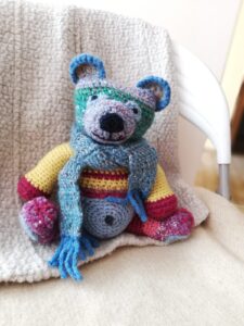 Picture of a cuddly toy mouse sitting on a comfortable blanket on a chair.